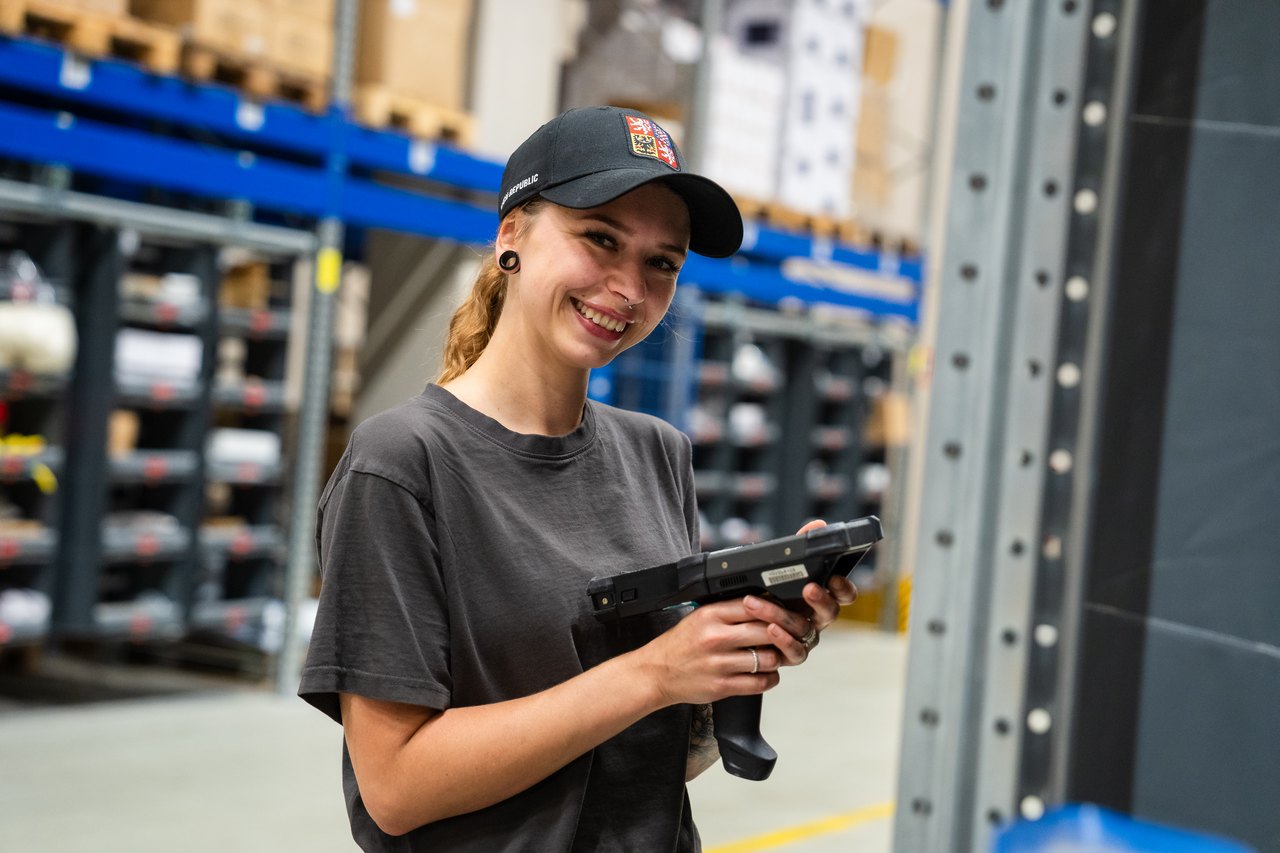 Lächelnde Frau mit dunklem Dutt und Nasenring in weißem T-Shirt.
